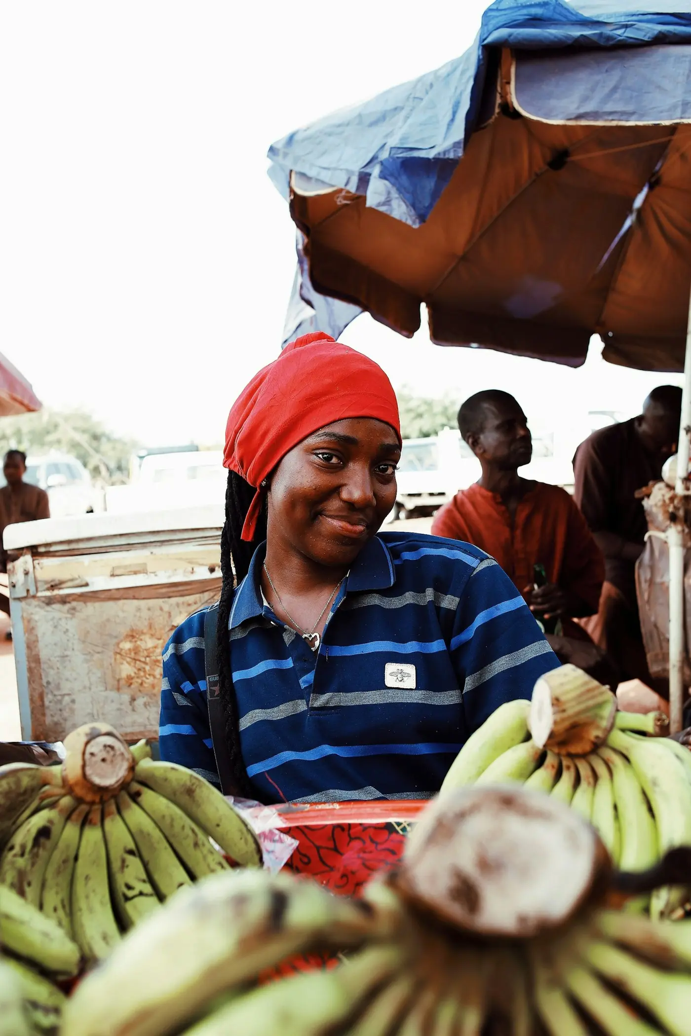 A market vendor in a red headscarf smiling at her stall